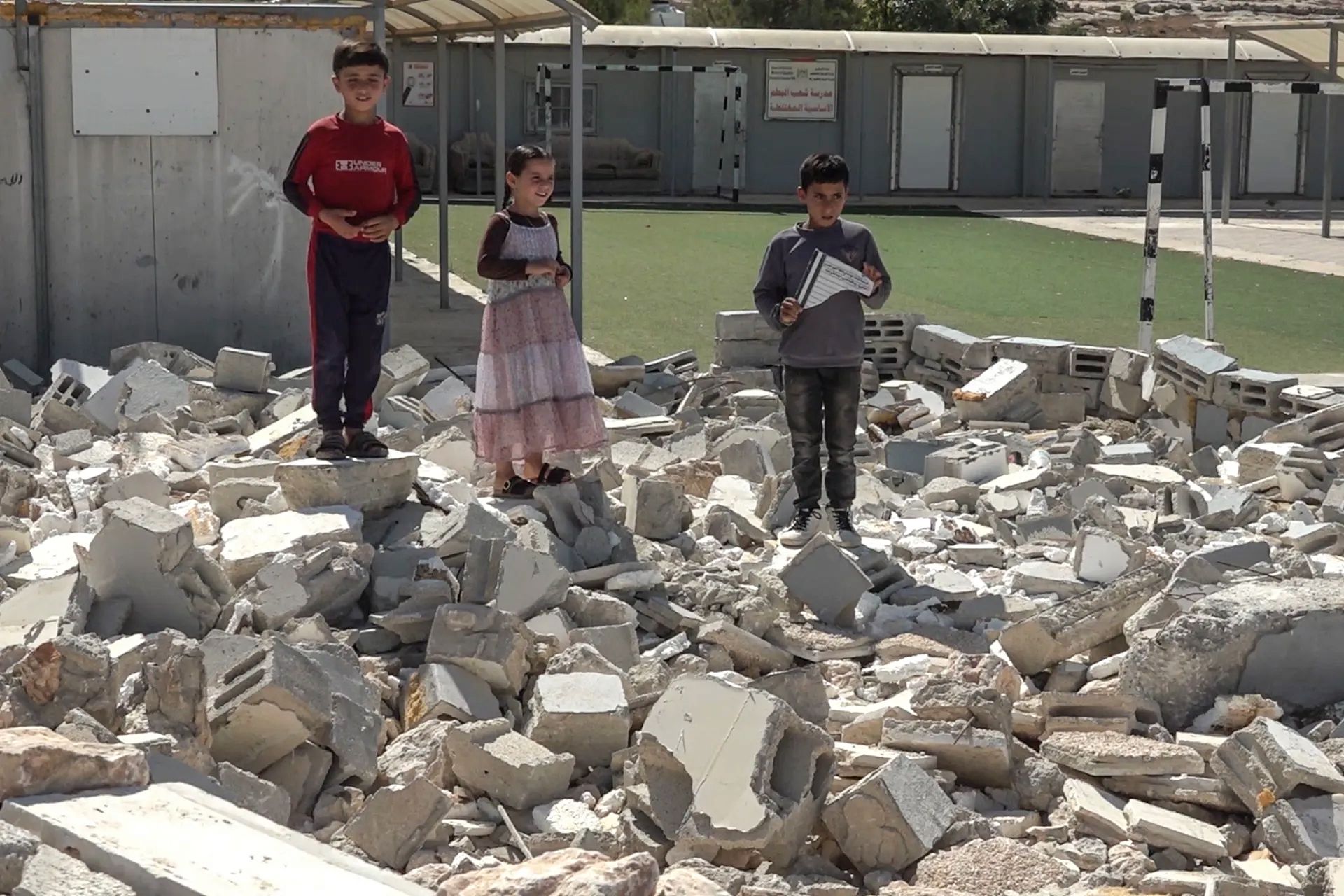 Children return to a damaged school under demolition threat